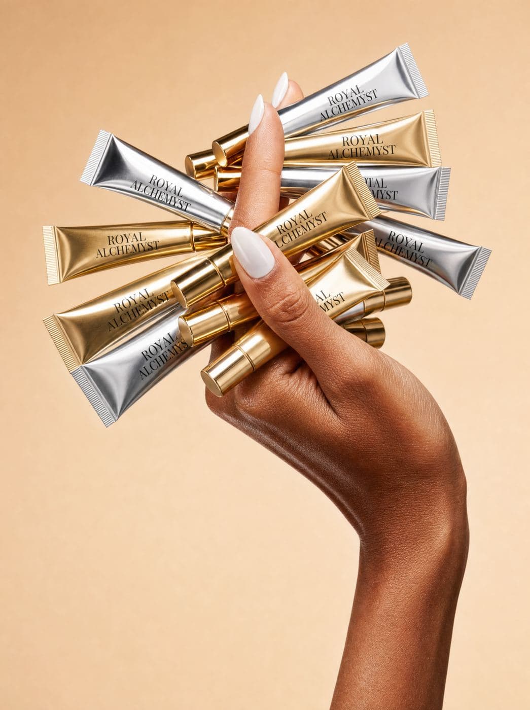 A hand holding a fan of gold and silver Royal Alchemyst squalane lip oils
